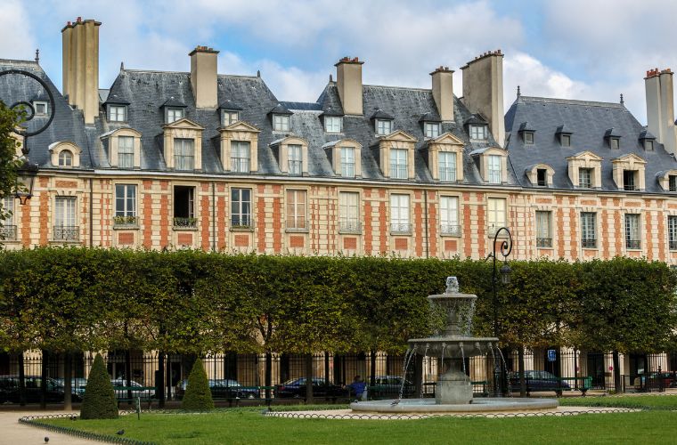 Le Marais bölgesinde, tarihi Paris binalarının ve dar sokakların yer aldığı nostaljik bir sokak görüntüsü. Kaldırım kafeleri ve pencerelerdeki çiçekler ile Paris’in yerel yaşam tarzını yansıtan bir sahne.